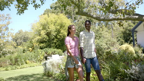 walking hand in hand, diverse couple enjoying sunny day in garden