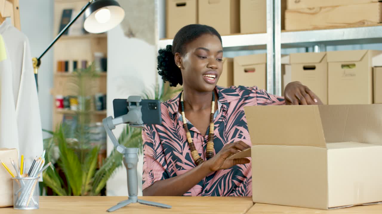 Close-up view young African American woman speaking on smartphone camera and recording video for blog in own clothing shop warehouse