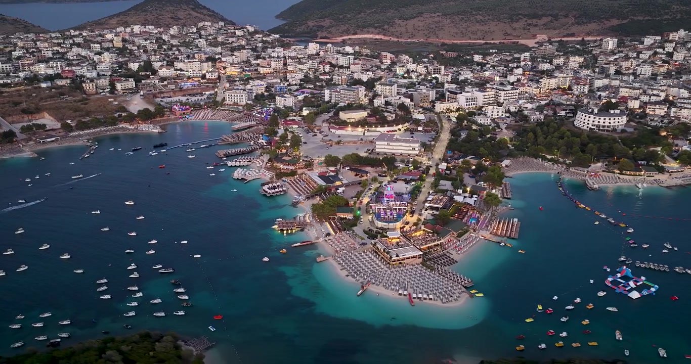 Vista aérea de drone da cidade turística e praia de Ksamil na Albânia, paisagem ao entardecer sobre uma baía de mar turquesa com muitos barcos