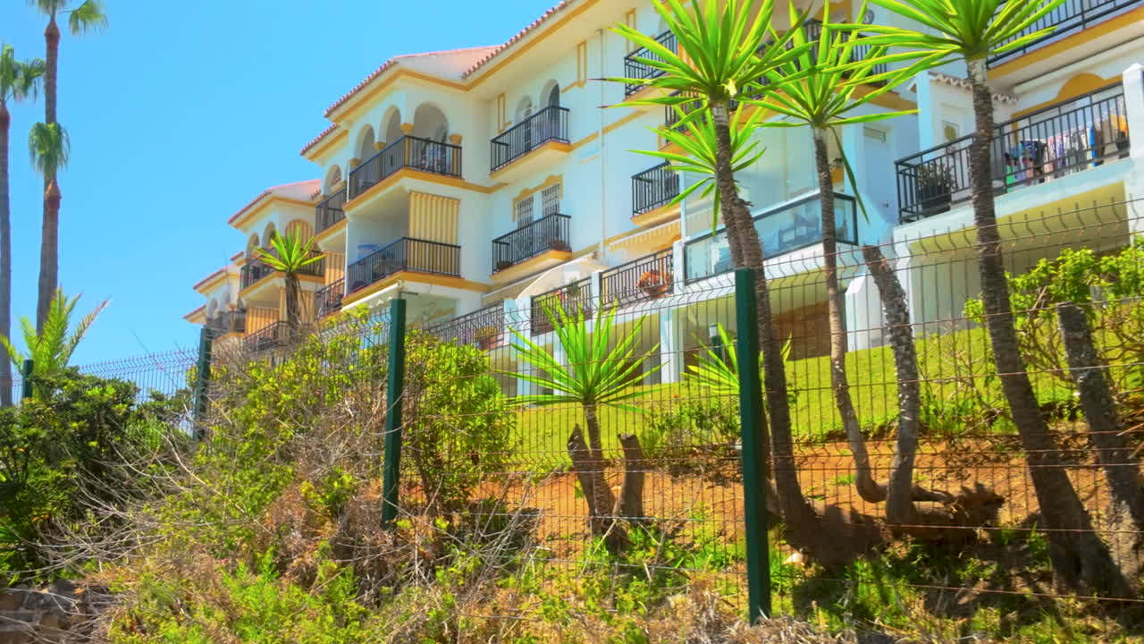 A residential building in Marbella, surrounded by greenery and palm trees, featuring traditional Mediterranean architectural elements like arched windows and balconies