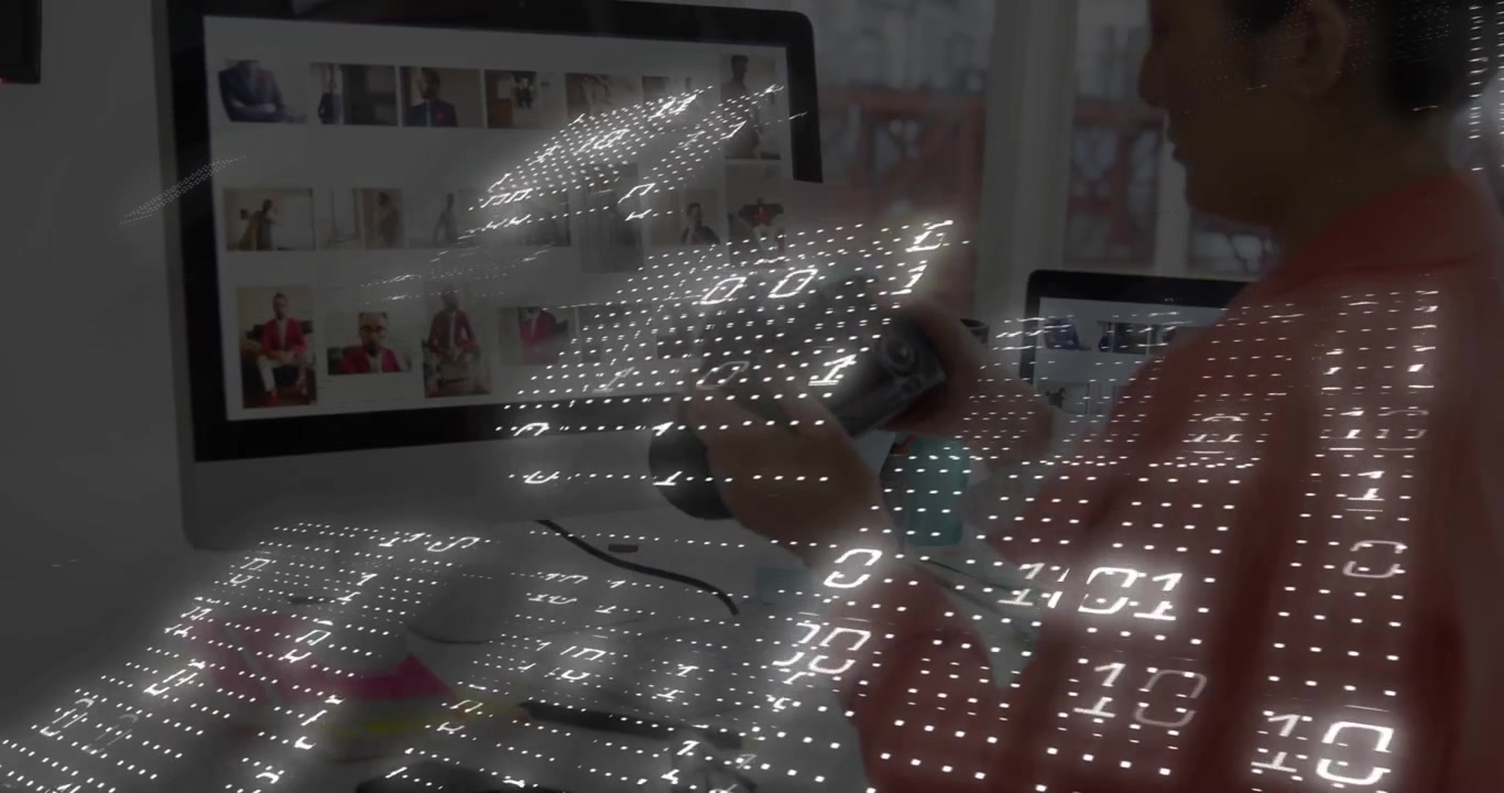 Woman at tech desk observing dotted overlay drifting over monitor, reaching phone to access gallery