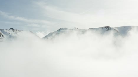 rise up out of a cloud to reveal a mountain top and ski stations with chairlifts