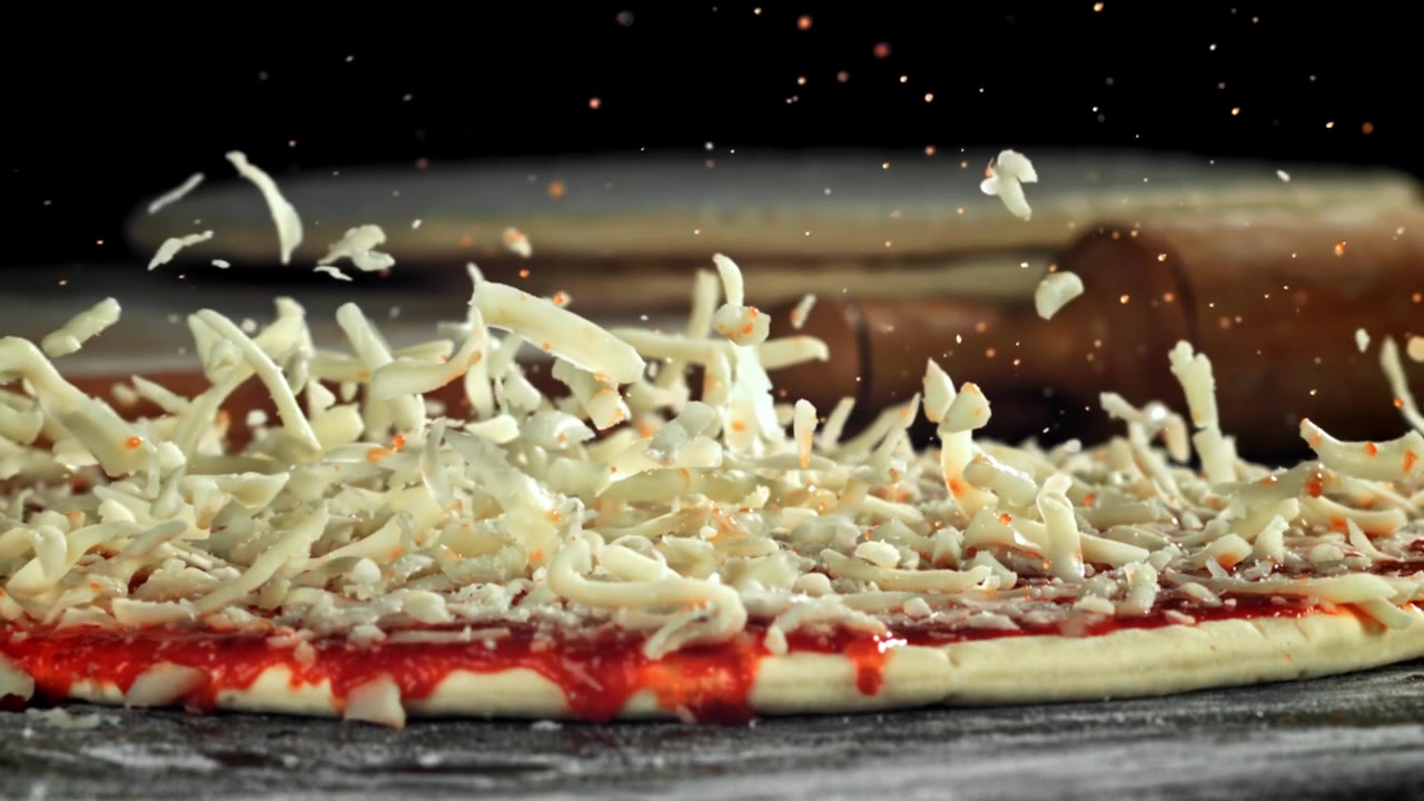Cospargere formaggio e spezie su un impasto per pizza al rallentatore