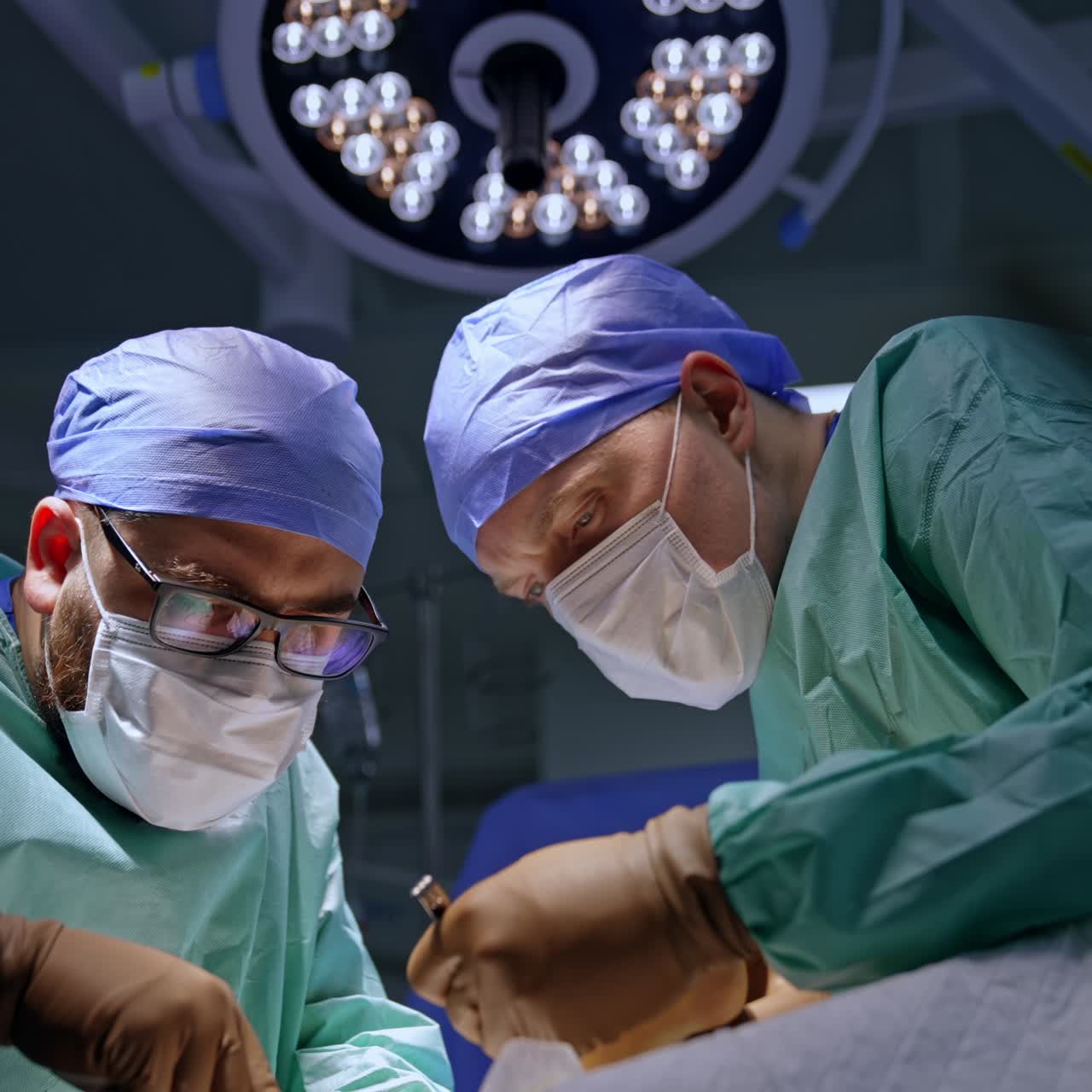 Experts in surgery stand on two sides from a patient. Concentrated doctors perform operation. Low angle view