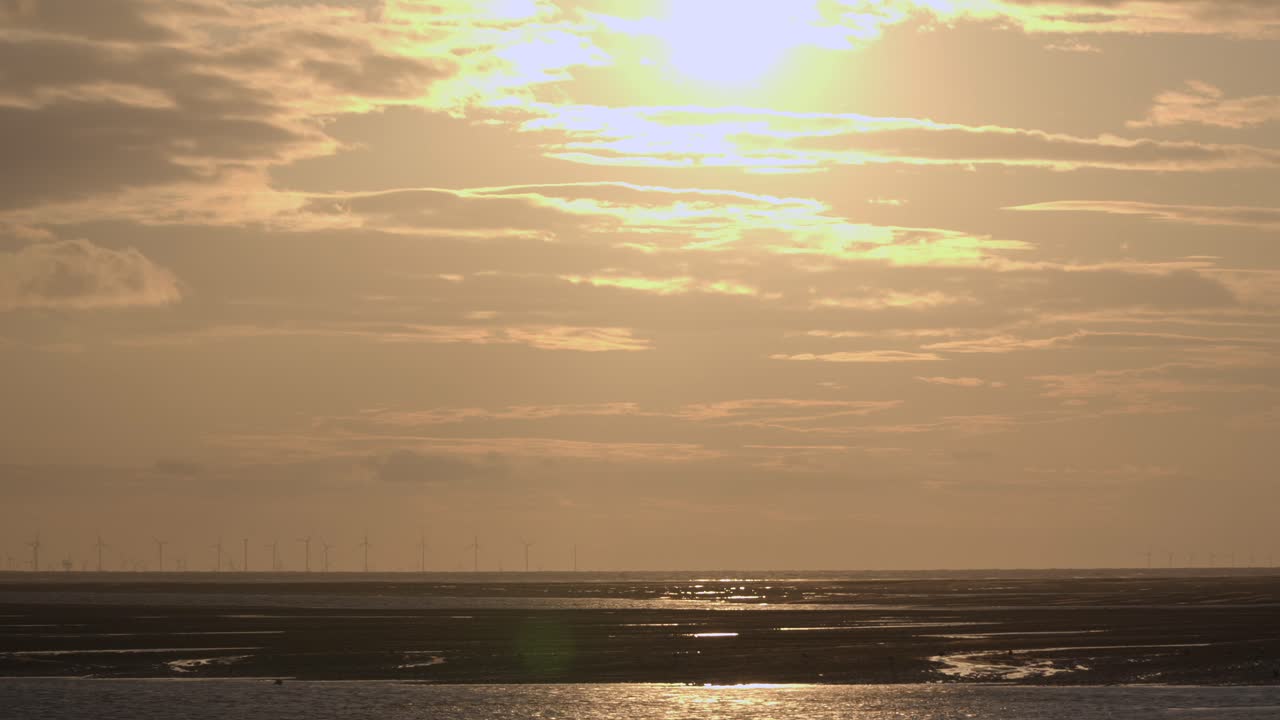 황금 태양은 상단 프레임에서 구름과 함께 두 방향으로 이동하고 지평선에 풍력 농장