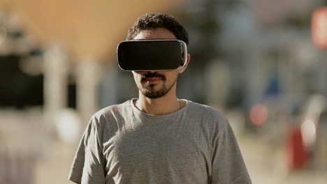 Joven-árabe-Con-Pelo-Rizado-Oscuro-Y-Barba-Con-Camiseta-Gris-En-El-Parque-Con-Gafas-De-Realidad-Virtual