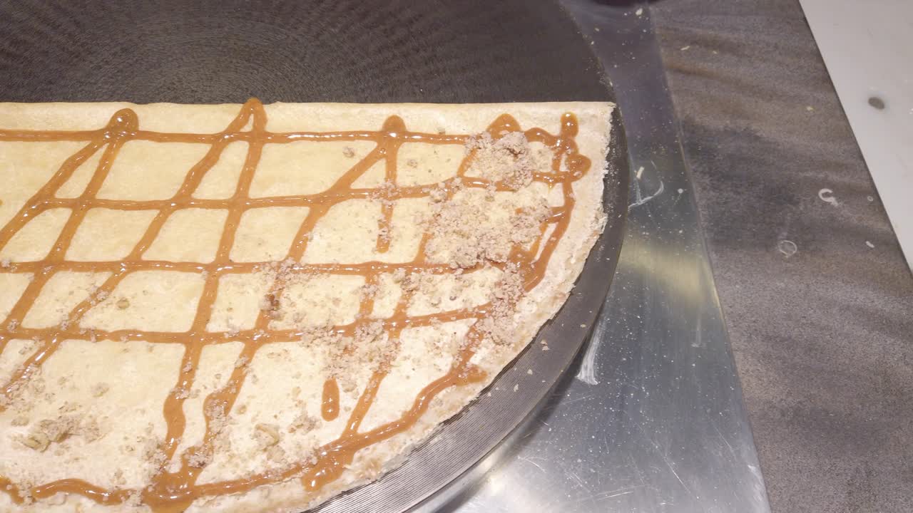 Pan shot of cook's hand pouring dough on a pancake with caramel on it, handheld shot