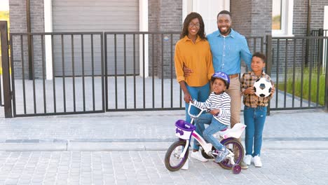 Porträt-Einer-Glücklichen-Afroamerikanischen-Familie-Mit-Kleinen-Kindern,-Die-Auf-Der-Straße-In-Der-Nähe-Des-Hauses-In-Einem-Vorort-Stehen-Und-In-Die-Kamera-Lächeln