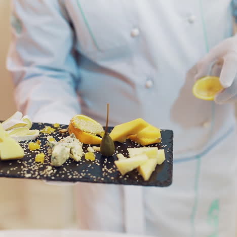 serving different types of hard cheese with lemon and sesame on the background of black wooden board in the cafe. close-up.