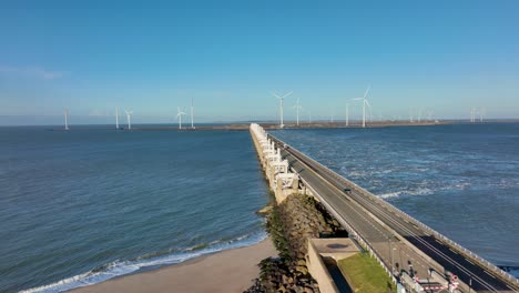 aerial slow motion shot of sparse traffic on the open eastern scheldt storm surge barrier and wind turbines in zeeland, the netherlands on a beautiful sunny day