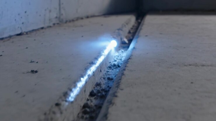 Appearing lower-left, blue point traveling along concrete joint toward corner, sparking rubble