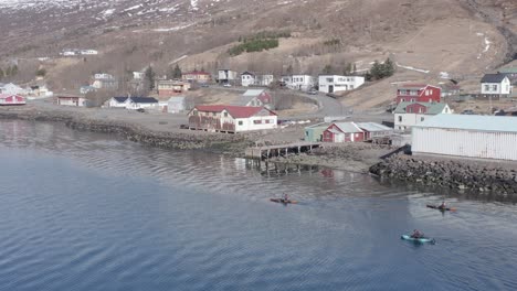 Kayakers-at-shore-of-rural-town-Eskifjördur-returning-from-adventure-trip-in-fjord,-aerial