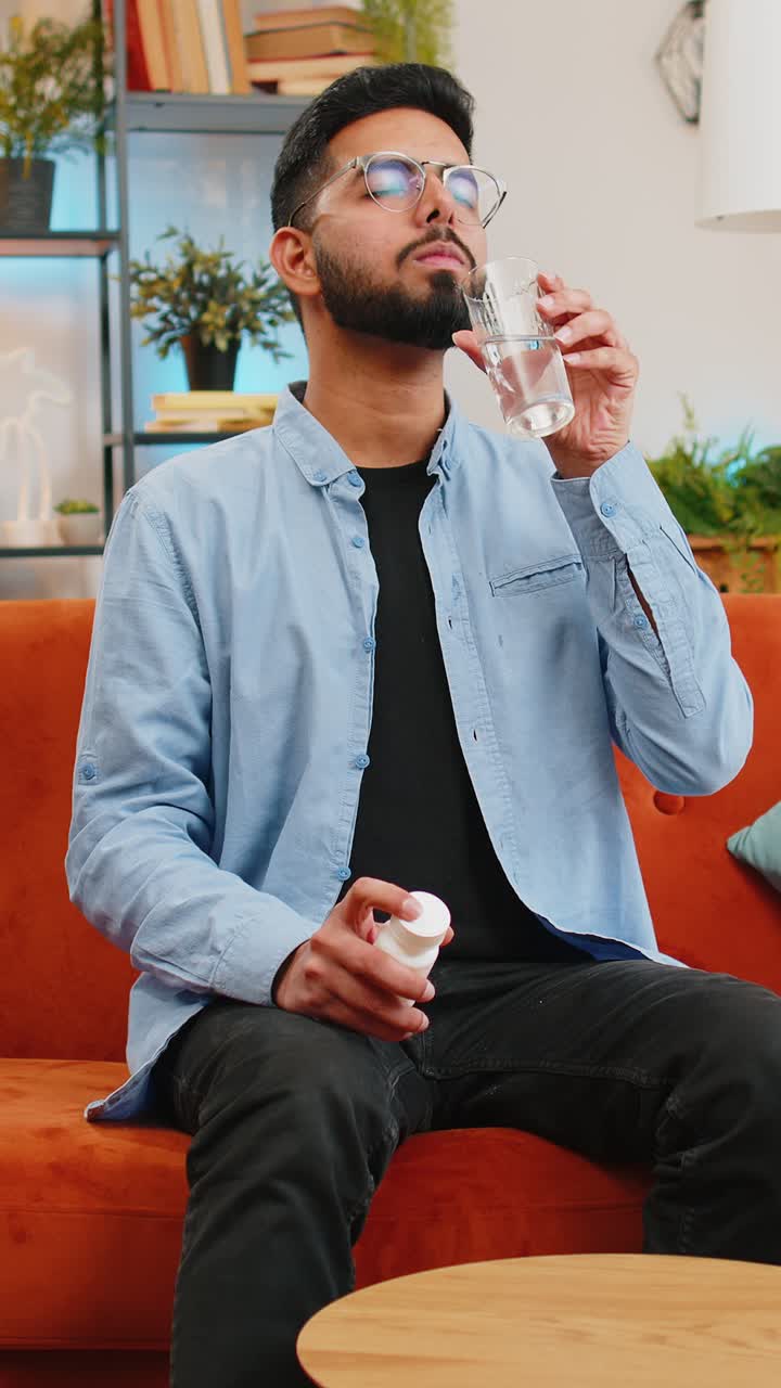 아픈 인디언은 약을 먹고, 물과 함께 항생제, 집에서 소파, 건강 관리, 약국에서 약을 먹습니다.