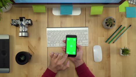 flat lay of man hands using phone with green screen at workplace