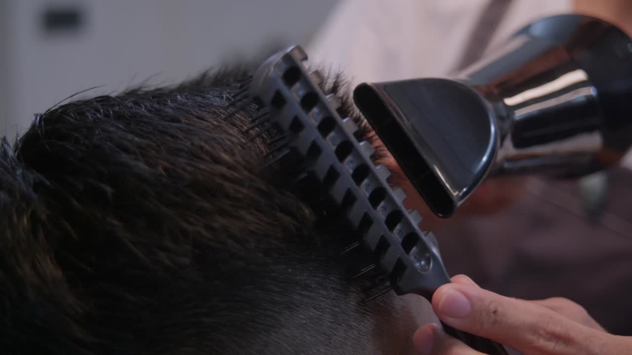Black hair dryer and black comb driven through top of head with black hair, filmed as closeup shot in slow motion handheld style