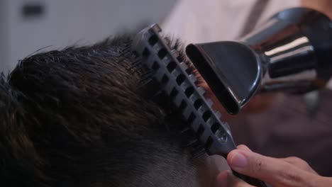 secador de cabello negro y peine negro impulsado a través de la parte superior de la cabeza con cabello negro, filmado como un primer plano en movimiento lento estilo portátil