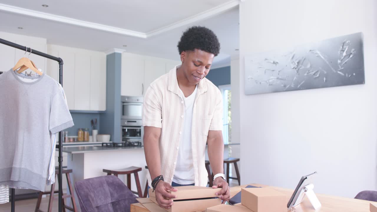 Mann richtet Karton aus, öffnet und faltet den Deckel, prüft die Bestellung auf dem Tablet und stapelt Pakete für den E-Commerce.