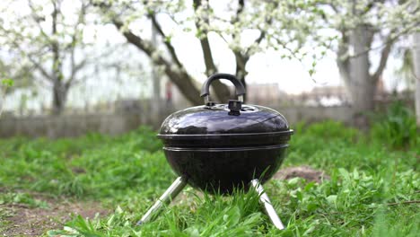 A-metal-barbecue-grill-stands-in-the-backyard-on-the-ground-with-grass-by-the-bushes