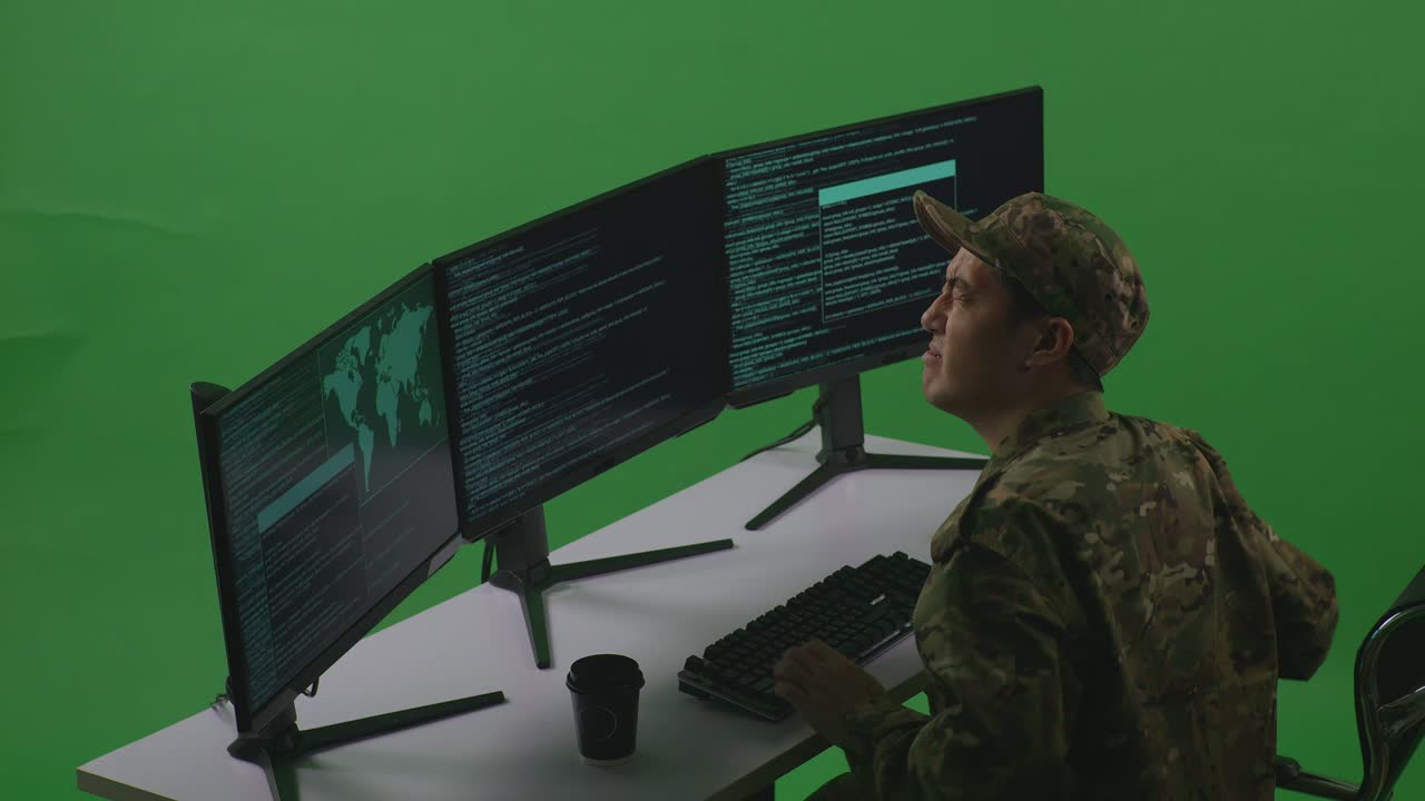 Side View Of Asian Man Soldier Developer Having Backache While Write Code With Multiple Computer Screens In Green Screen Studio