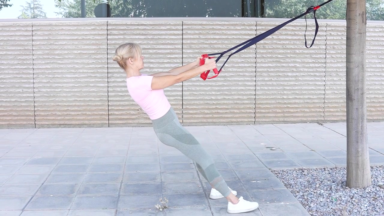 A blonde woman is doing outdoor trx suspension training for her fitness commitment