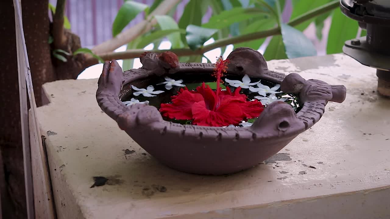 agua sagrada espiritual con flor de hibisco mantenida para las aves en la entrada de la casa desde un ángulo diferente