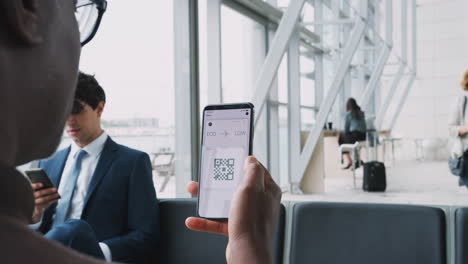 Close-Up-Of-Businessman-In-Airport-Departure-Lounge-Looking-At-E-Ticket-On-Mobile-Phone-Screen