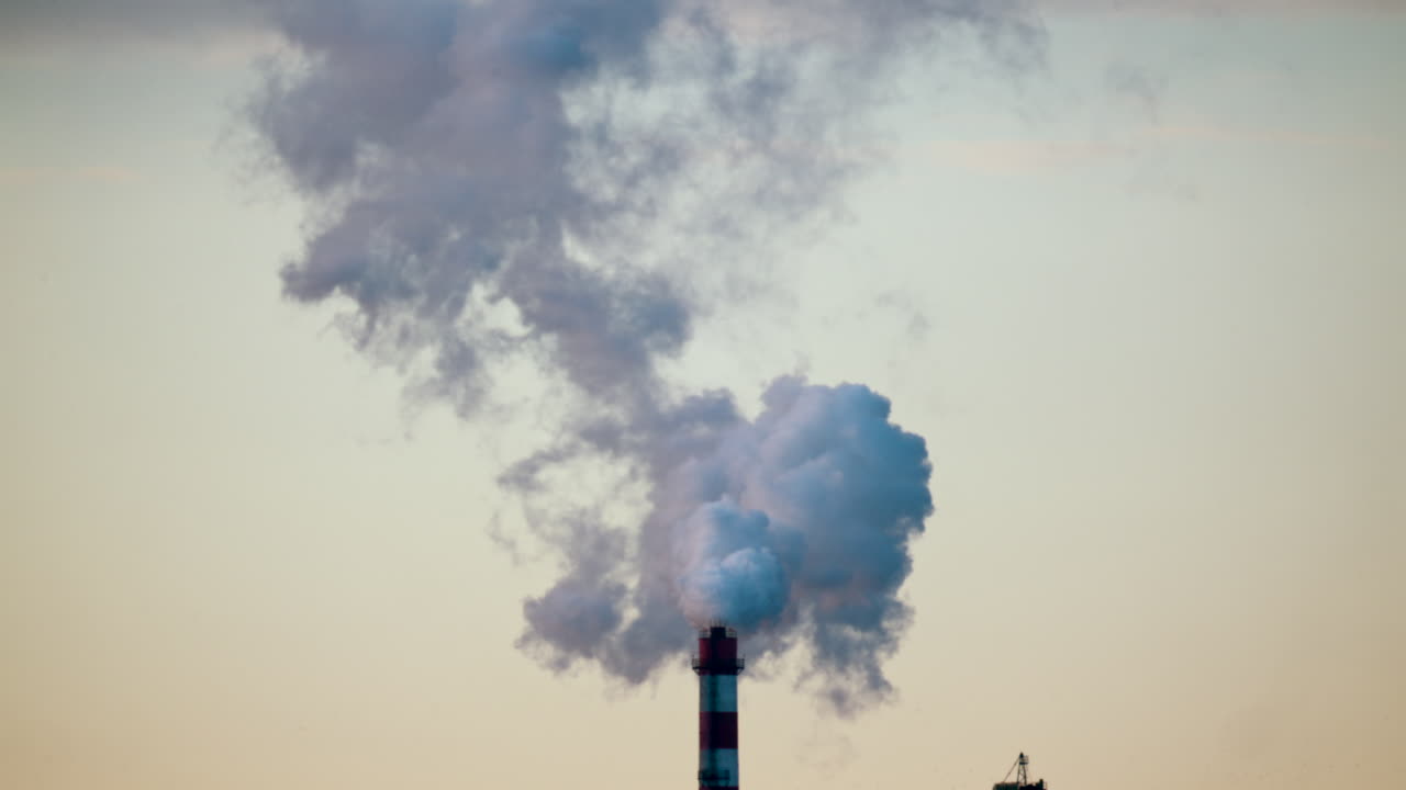 Ciminiera industriale che rilascia fumo denso nel cielo sopra un cantiere edile cittadino.