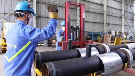 workers transporting heavy pipeworks with manual forklift in warehouse