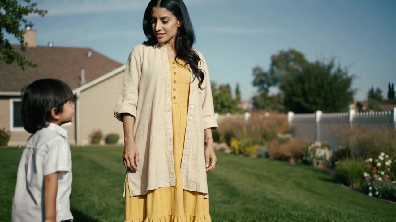 Running son greeting mother in yellow dress on lawn, causing her stopping, smiling by picket fence