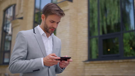 Man-using-mobile-phone-on-move-outdoors.-Manager-looking-cellphone-on-street.