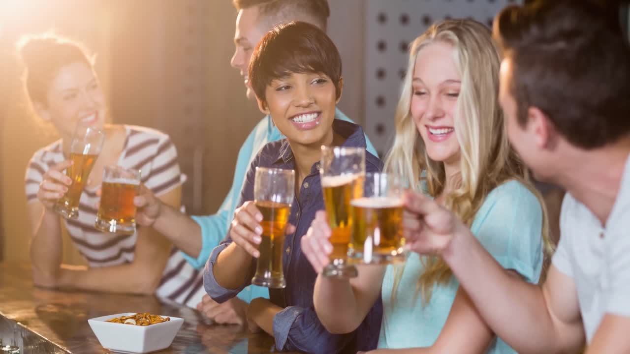 felices amigos femeninos y masculinos diversos hablando, sosteniendo bebidas y haciendo un brindis en el bar