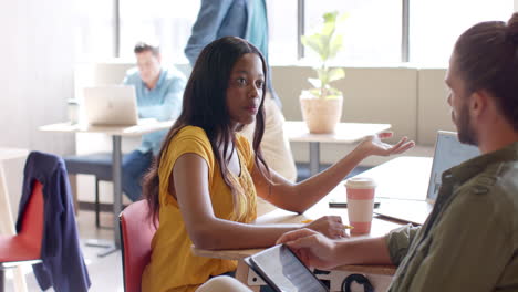 young african american woman discusses with a young caucasian man in a casual business setting in an