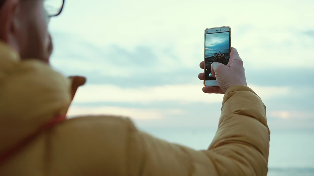 persona tomando una foto de la puesta de sol en la costa