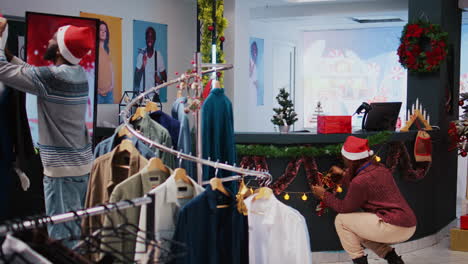 african american coworkers setting up christmas decorations in shopping mall clothing store. employees in festive spirit mood, ornating fashion boutique with xmas ornaments