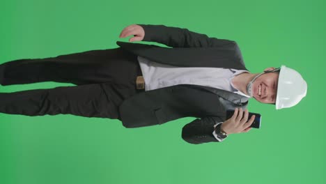 asian chief engineer in the hard hat having video call on mobile phone while walking on green screen chroma key