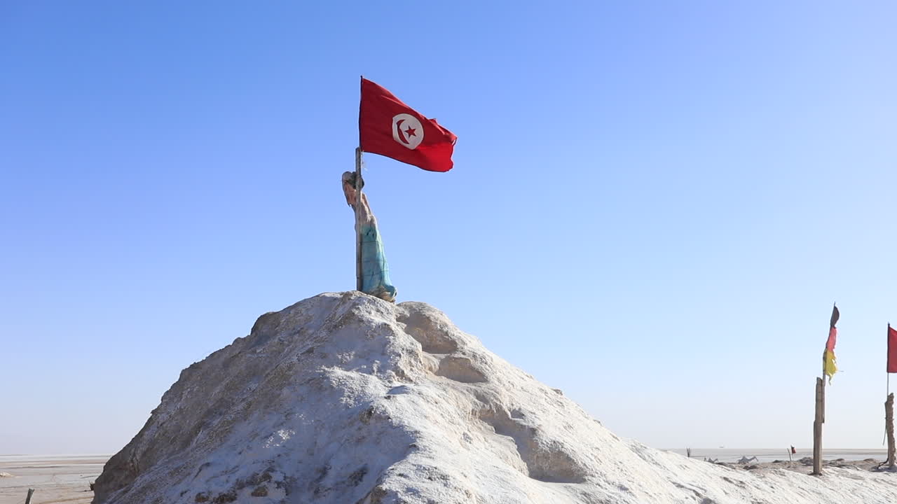 Statue holding Tunisian flag atop salt hill in Chott el Jerid desert under clear sky