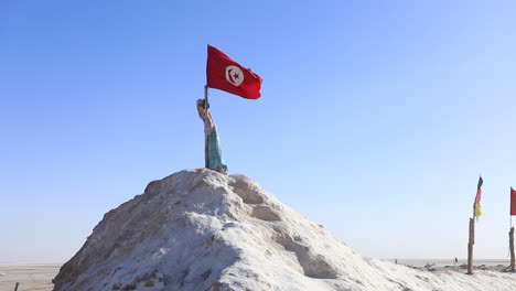 statue holding tunisian flag atop salt hill in chott el jerid desert under clear sky