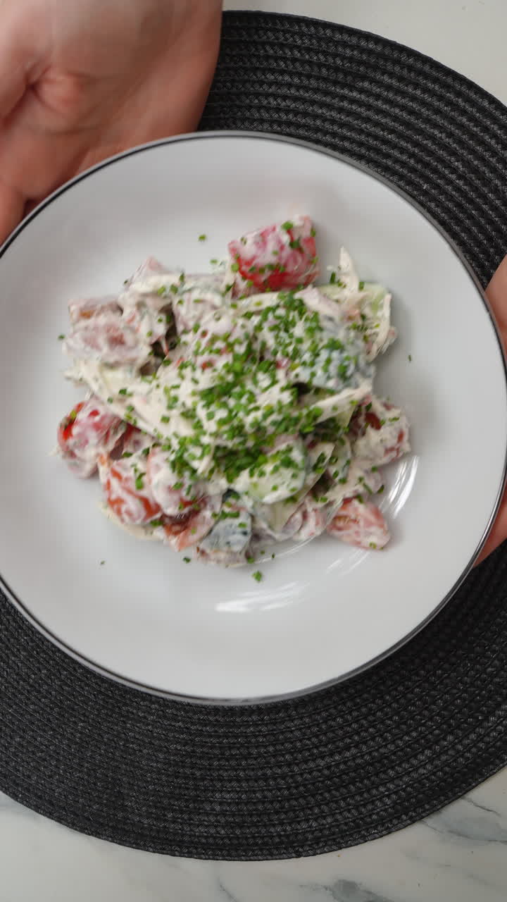 Vertical footage Professional chef's hands preparing summer salad with crisp lettuce, ripe tomato, cucumber, drizzling chive cream sauce on pristine white plate