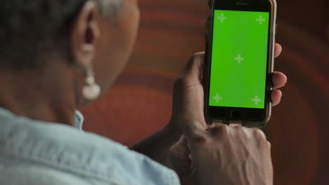 atractiva mujer negra de edad avanzada deslizando su dedo en un teléfono móvil de pantalla verde