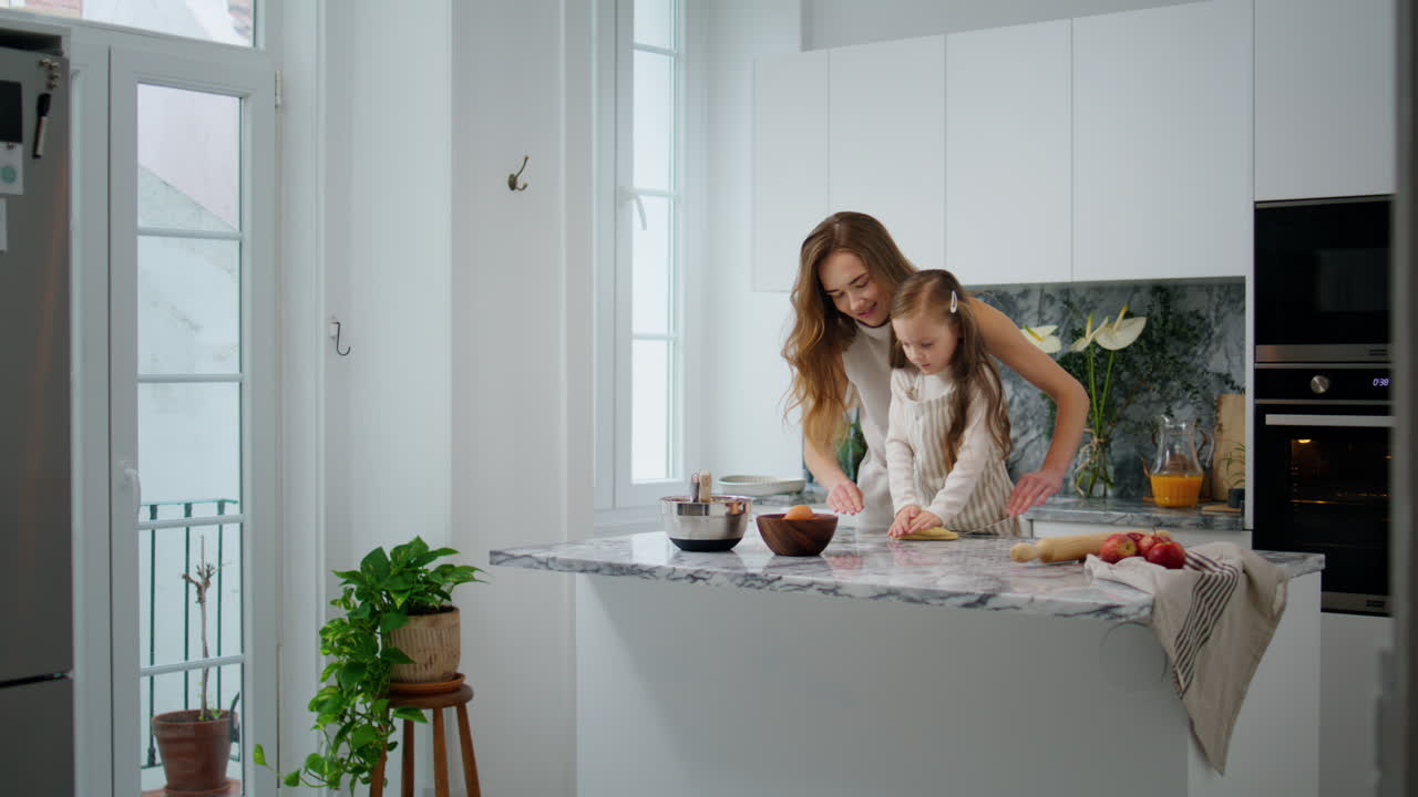 Famiglia carina che stende l'impasto in casa. Madre e figlia affettuose che impastano in cucina.