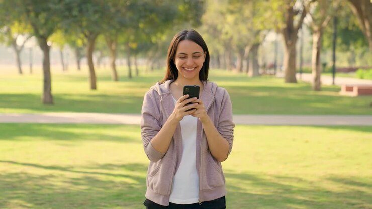 feliz niña india usando un teléfono móvil en invierno al aire libre en un parque por la mañana