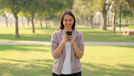 feliz niña india usando un teléfono móvil en invierno al aire libre en un parque por la mañana
