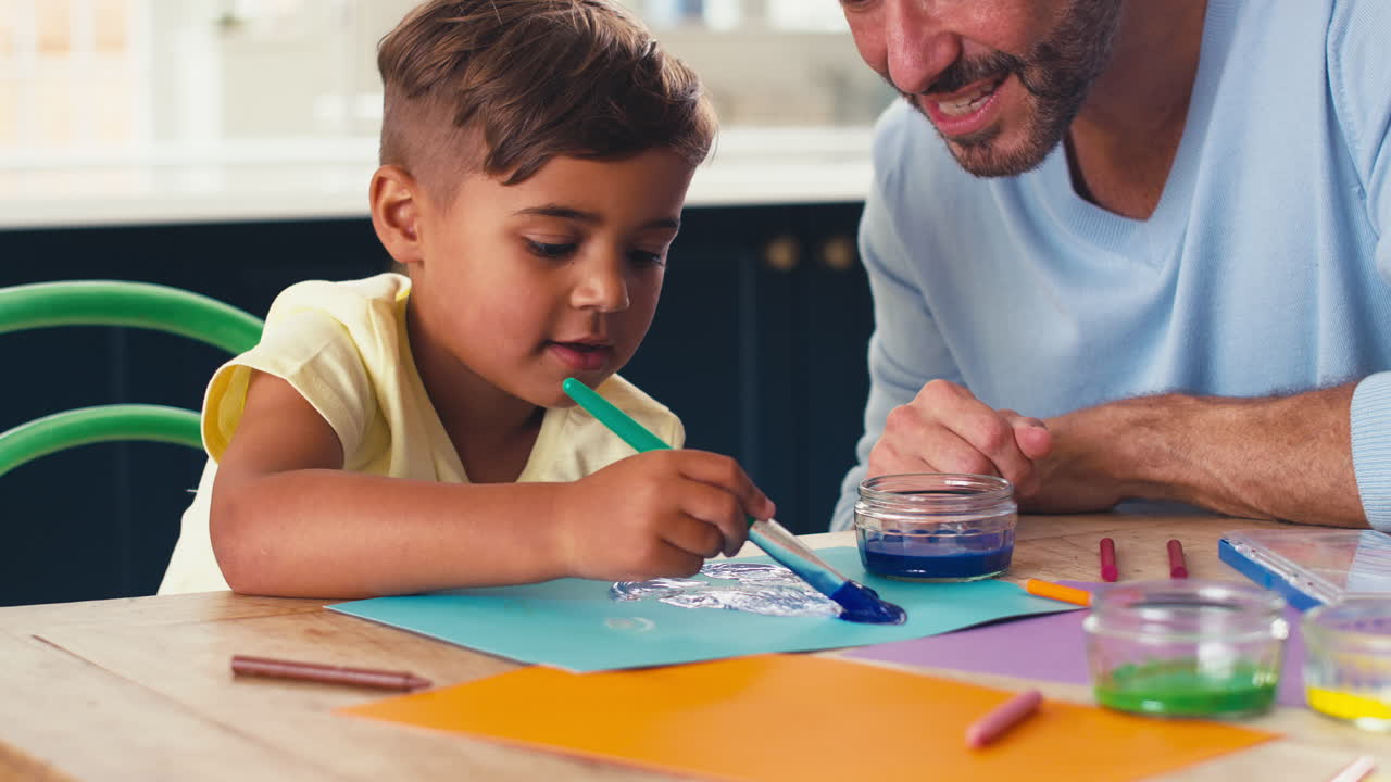 padre maduro en casa en la cocina con su hijo pintando una imagen juntos