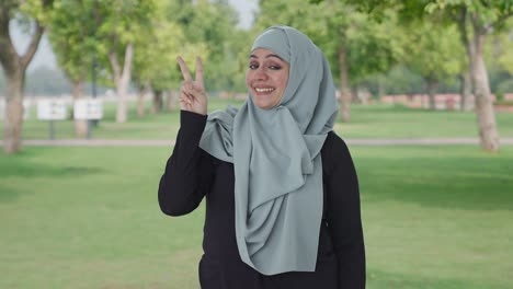 happy muslim woman showing victory sign in park