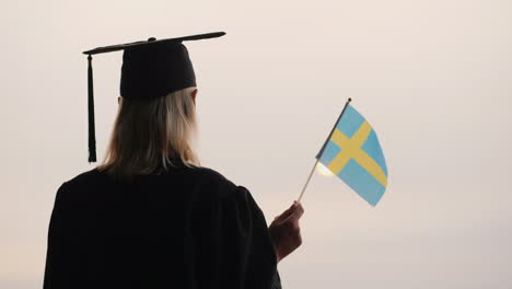 Rückansicht-Eines-Absolventen-Mit-Der-Flagge-Von-Schweden-In-Der-Hand-Studieren-In-Norwegen