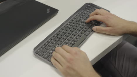 a man is typing on a computer keyboard, white desk