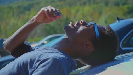 an eye-level shot of a handsome, slender young man snacking on popcorn under a beautiful sunny day in a parking lot