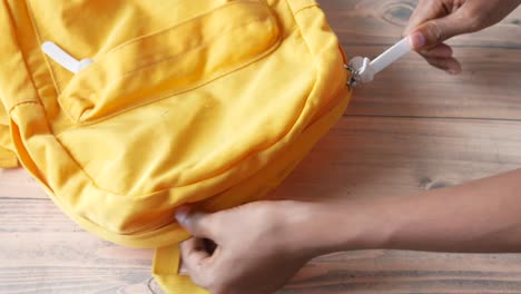 person adjusting zipper on a yellow backpack