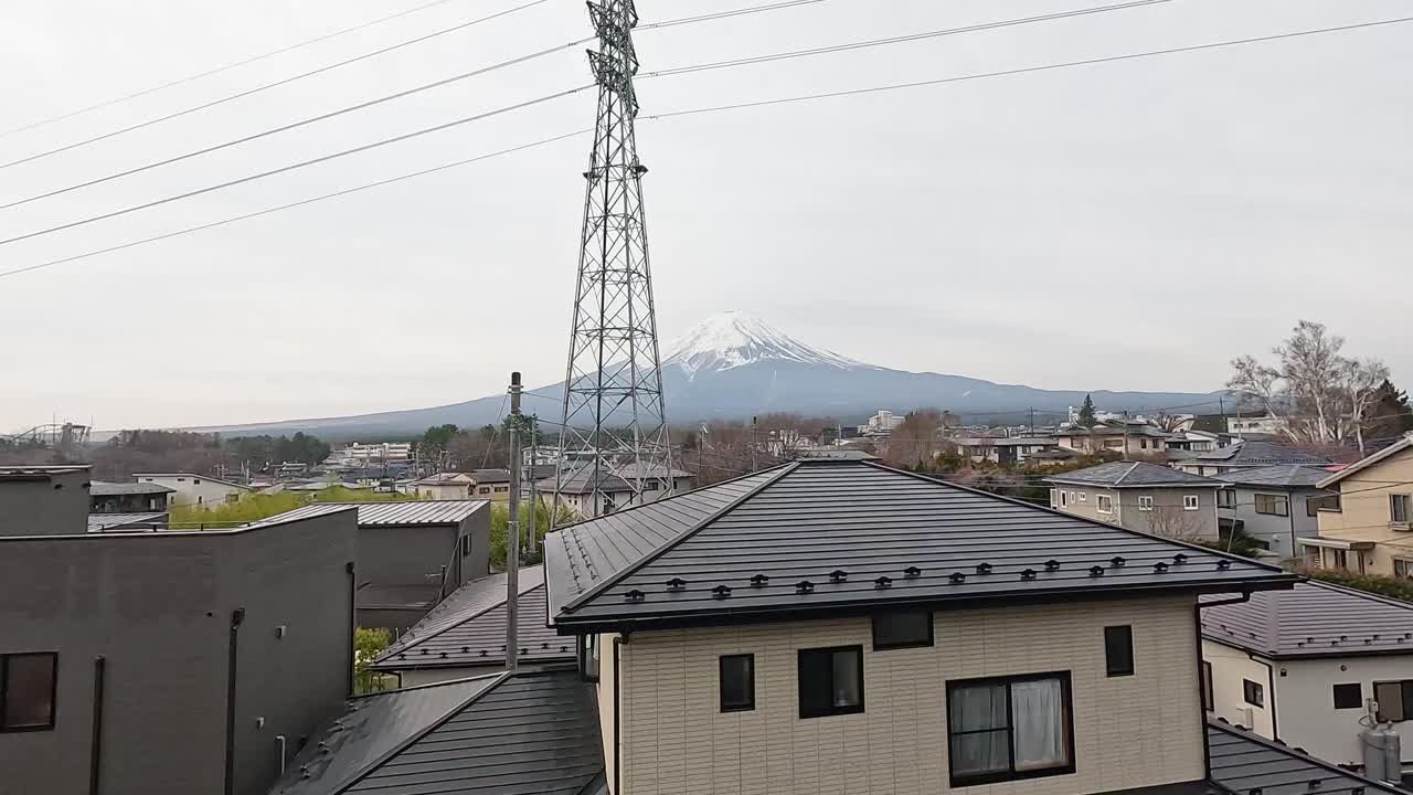 A serene view of Mount Fuji over a residential area in Kawaguchiko, Japan, captured on a cloudy day with static camera framing