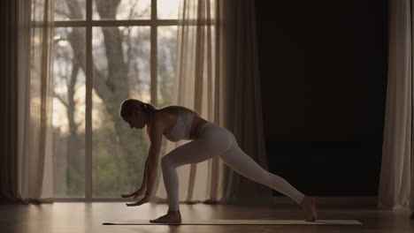 slow motion: young woman is doing yoga in a white room filled with light the girl performs yoga stands and elements near the large window.